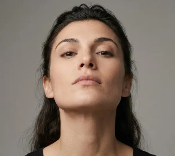 Close-up of a person's face with chin raised and head tilted back slightly — eyes looking forward and slightly downward from elevated angle, expression conveying confidence and dominance